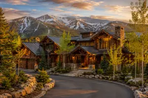 Beautifully restored luxury log home in Vail, CO at golden hour with stone accents, rich wood finishes, evergreens, aspens, and snow-dusted mountain views